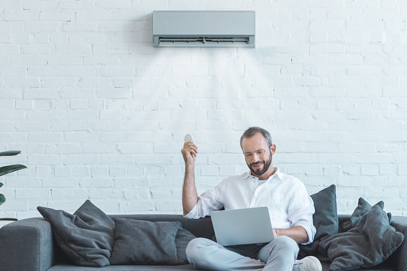 Man sitting on couch using remote to control ductless AC.